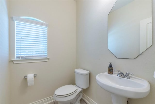 half bathroom featuring baseboards, a sink, and toilet