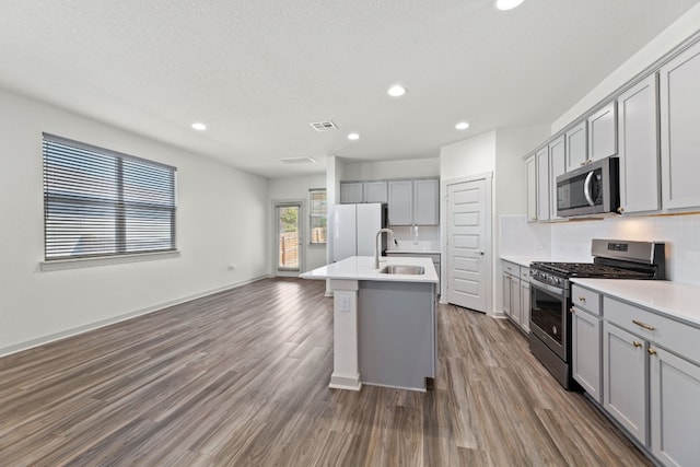 kitchen featuring appliances with stainless steel finishes, sink, a kitchen island with sink, wood-type flooring, and gray cabinets