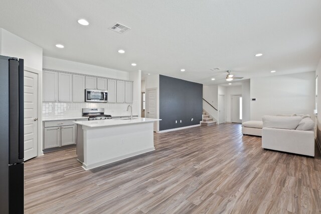 kitchen with stainless steel appliances, light hardwood / wood-style floors, a center island with sink, gray cabinetry, and ceiling fan