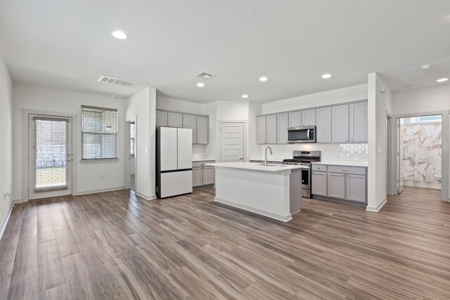 kitchen featuring appliances with stainless steel finishes, sink, a kitchen island with sink, wood-type flooring, and gray cabinets