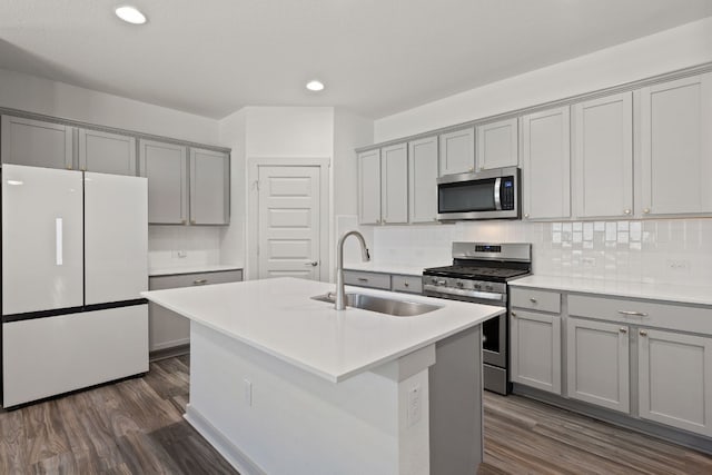 kitchen with dark hardwood / wood-style floors, stainless steel appliances, gray cabinets, and a center island with sink