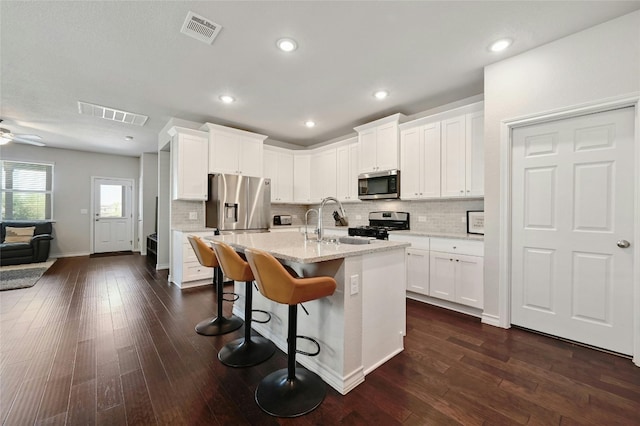 kitchen with decorative backsplash, an island with sink, dark hardwood / wood-style floors, ceiling fan, and stainless steel appliances