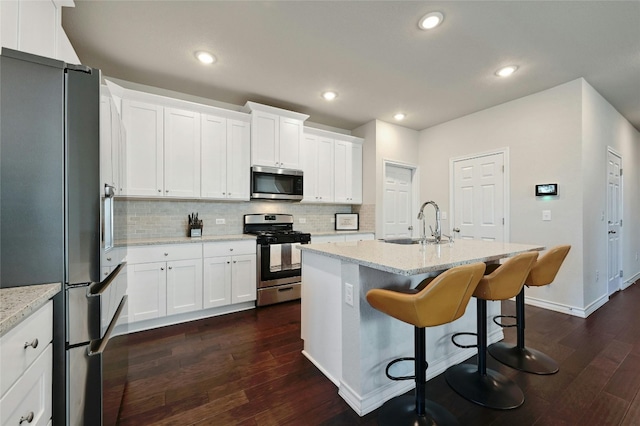 kitchen with backsplash, dark hardwood / wood-style flooring, appliances with stainless steel finishes, light stone countertops, and a center island with sink