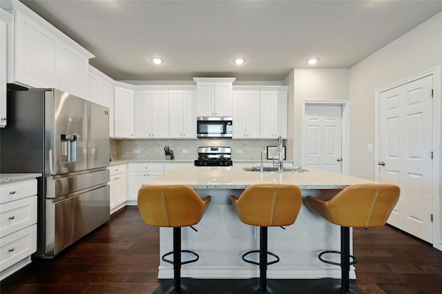 kitchen with appliances with stainless steel finishes, tasteful backsplash, a center island with sink, and dark hardwood / wood-style flooring