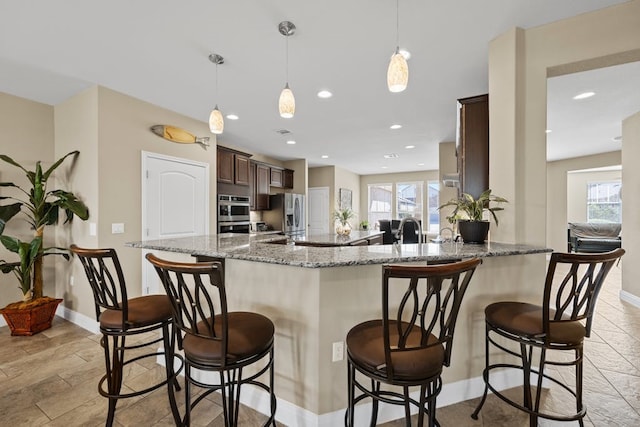 kitchen with a peninsula, stone counters, a breakfast bar area, and dark brown cabinets