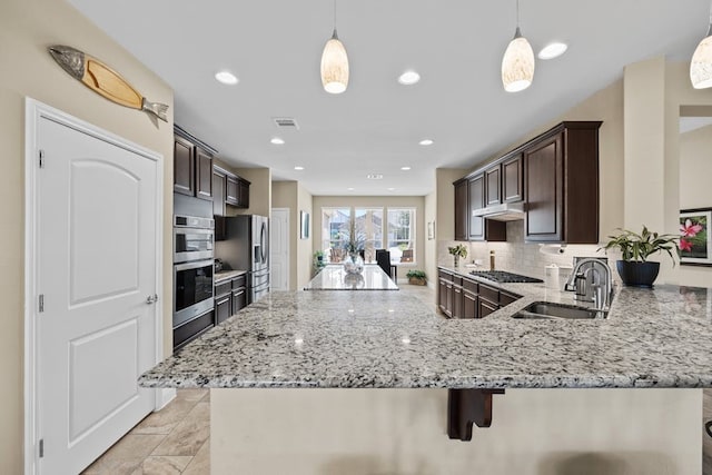 kitchen with pendant lighting, a sink, under cabinet range hood, and dark brown cabinetry