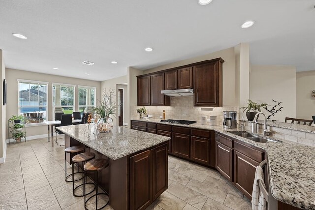 kitchen featuring sink, light tile patterned flooring, a kitchen island, and light stone countertops