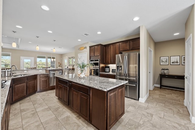 kitchen with appliances with stainless steel finishes, a kitchen island, sink, and light stone countertops