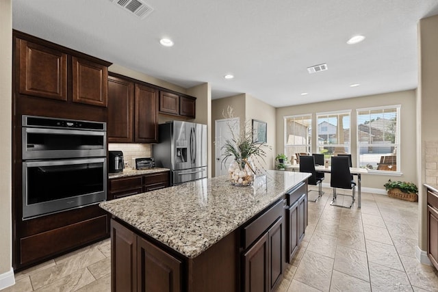 kitchen featuring tasteful backsplash, appliances with stainless steel finishes, light stone counters, light tile patterned floors, and a center island