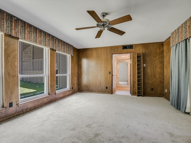 empty room with ceiling fan, wooden walls, and carpet floors