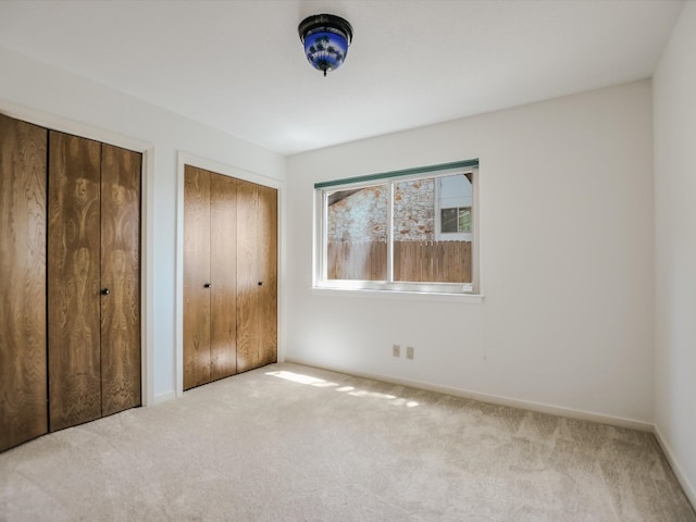 unfurnished bedroom with two closets and light carpet