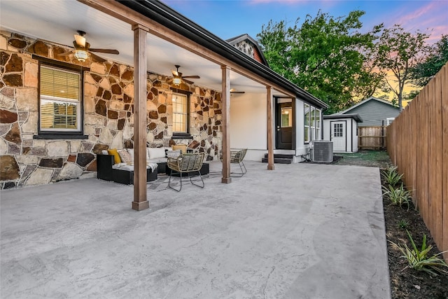 patio terrace at dusk featuring central air condition unit, outdoor lounge area, ceiling fan, and a shed