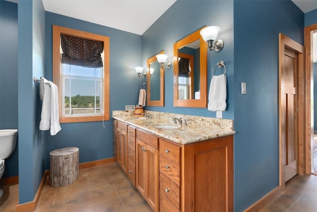 bathroom featuring baseboards, a sink, toilet, and double vanity