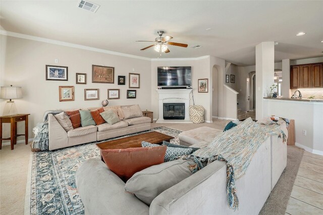 living room with ceiling fan, crown molding, and light colored carpet