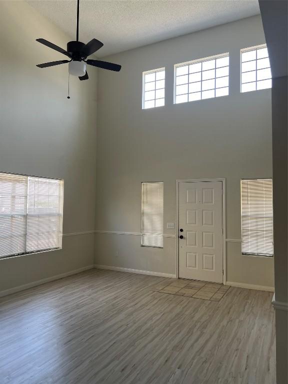 interior space featuring a textured ceiling, ceiling fan, a high ceiling, baseboards, and light wood-style floors