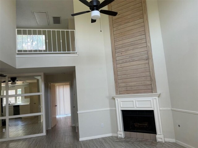 unfurnished living room with ceiling fan, a towering ceiling, and wood-type flooring