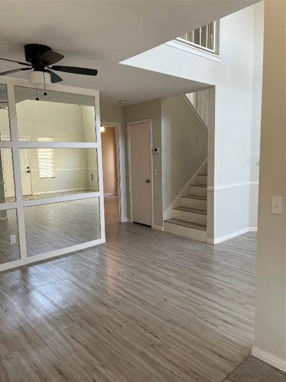 empty room with a ceiling fan, stairway, baseboards, and wood finished floors