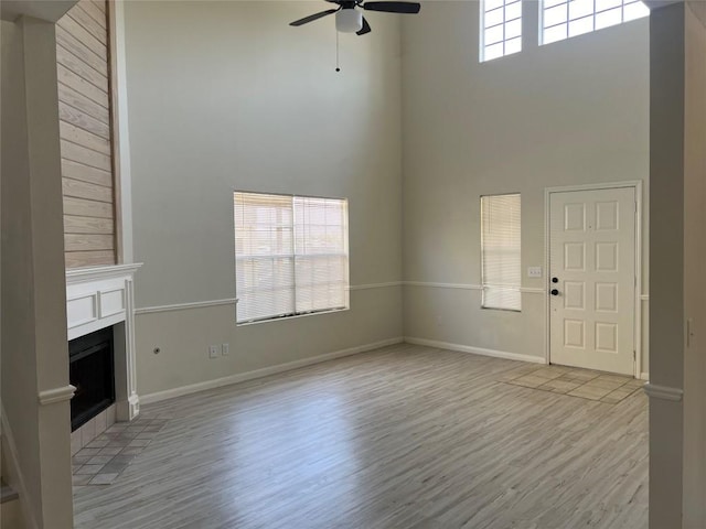 unfurnished living room featuring light wood finished floors, plenty of natural light, a high ceiling, and a fireplace with flush hearth