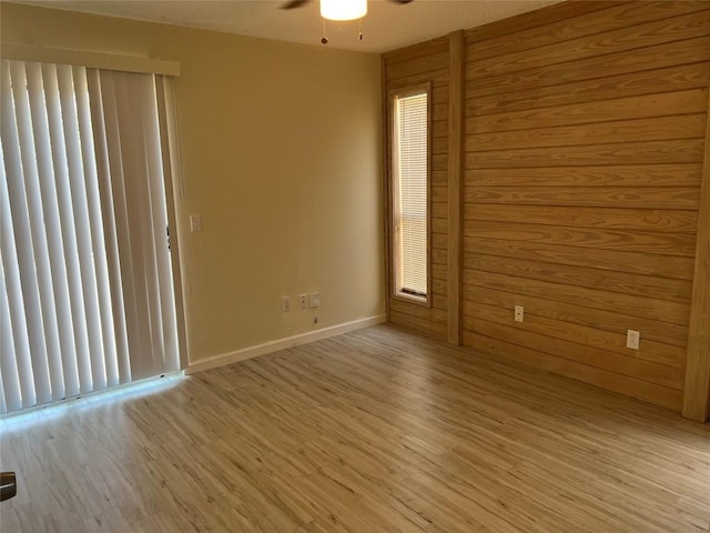 unfurnished room with wood walls, light wood-style flooring, baseboards, and ceiling fan