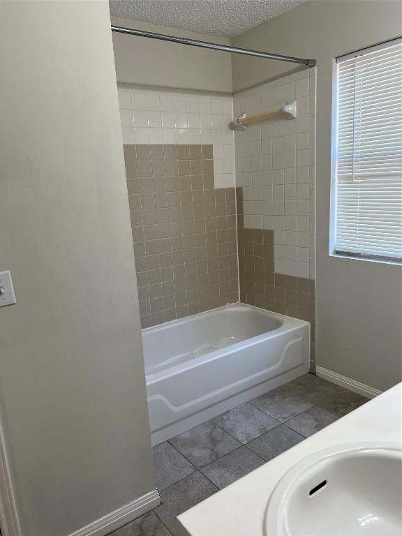 bathroom featuring baseboards, tile patterned flooring, bathtub / shower combination, a textured ceiling, and a sink