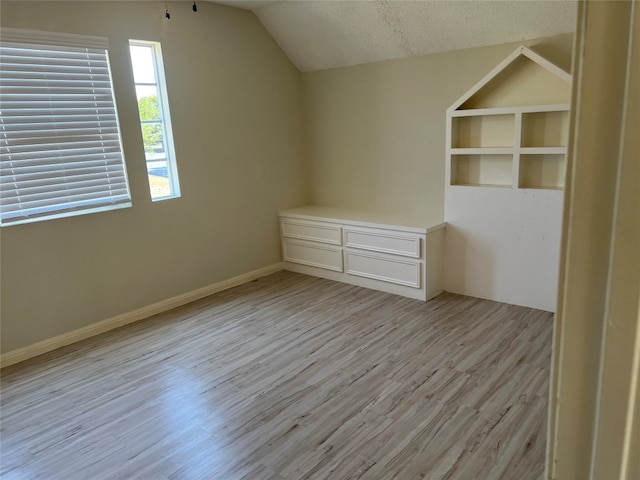 additional living space featuring a textured ceiling, built in features, light wood-type flooring, and lofted ceiling