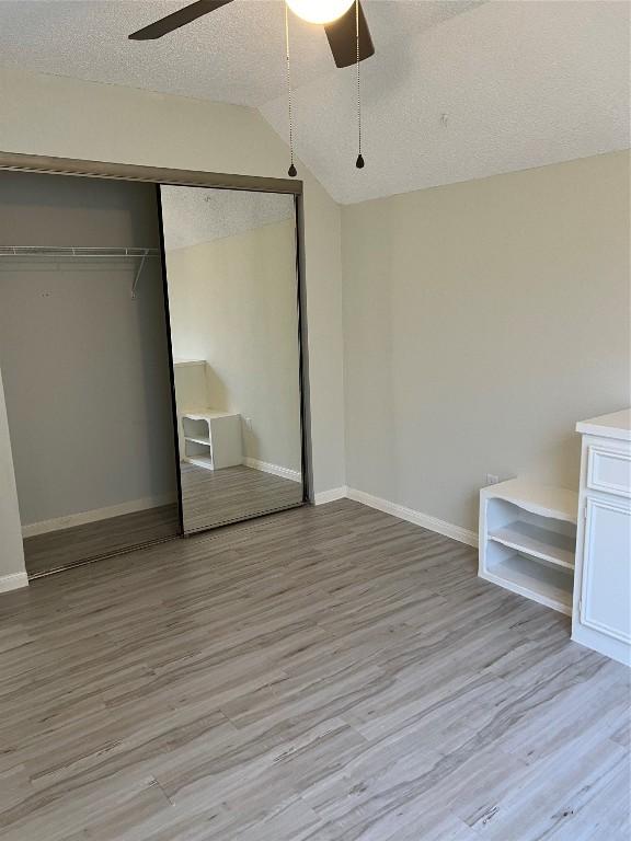 unfurnished bedroom featuring lofted ceiling, a textured ceiling, light wood-style flooring, baseboards, and a closet