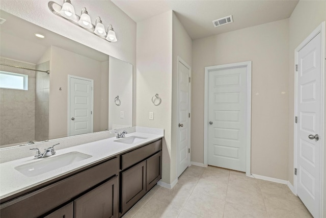 bathroom with tile patterned flooring, a tile shower, and vanity