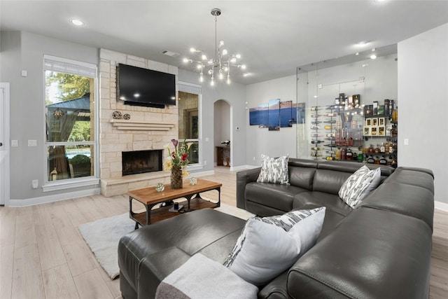 living room featuring light hardwood / wood-style floors, a stone fireplace, and an inviting chandelier