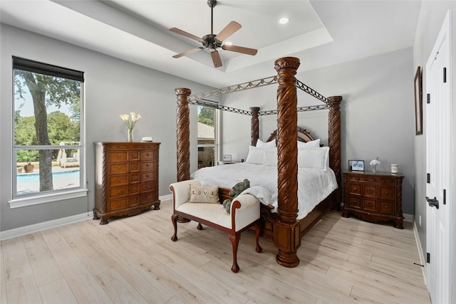 bedroom with a tray ceiling, multiple windows, ceiling fan, and light hardwood / wood-style flooring