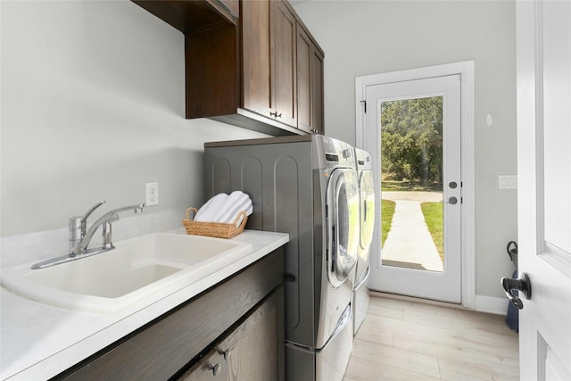 clothes washing area with washer and clothes dryer, light hardwood / wood-style flooring, cabinets, and sink