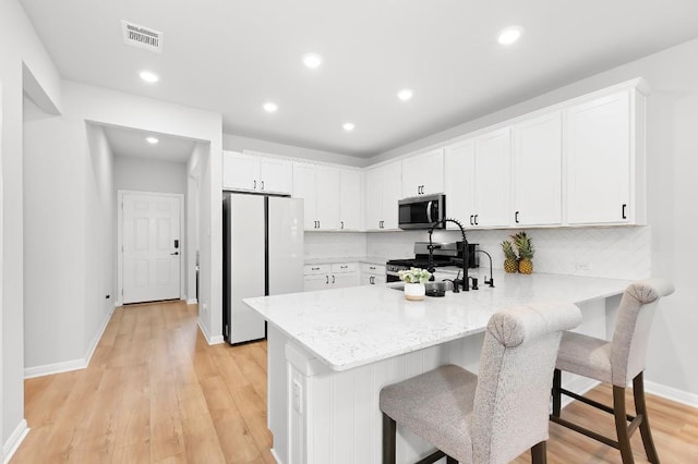 kitchen featuring kitchen peninsula, a kitchen breakfast bar, stainless steel appliances, and white cabinetry