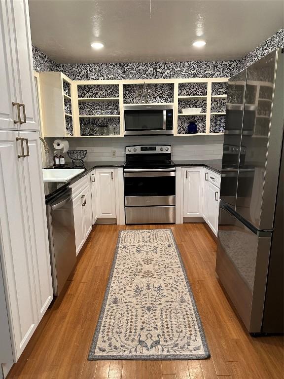 kitchen featuring appliances with stainless steel finishes, dark countertops, light wood-type flooring, and open shelves