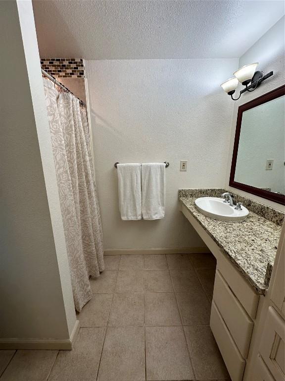 full bathroom with tile patterned flooring, a textured ceiling, baseboards, and a sink