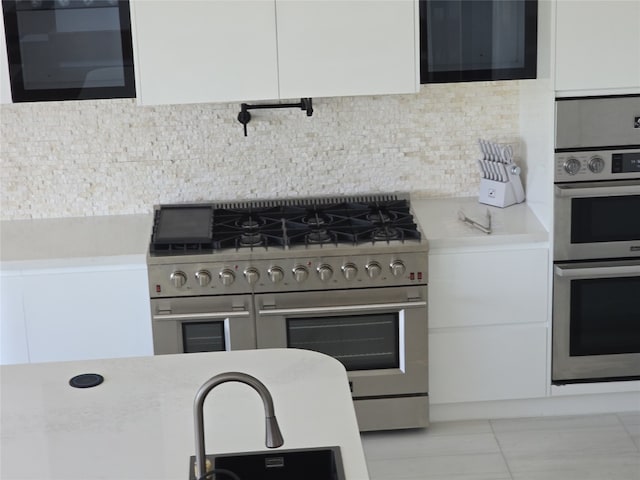 kitchen featuring white cabinets, light tile patterned floors, tasteful backsplash, and stainless steel appliances