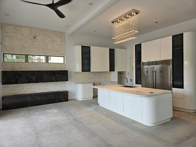 kitchen featuring beamed ceiling, sink, a center island with sink, white cabinetry, and built in fridge