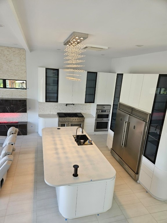 kitchen featuring appliances with stainless steel finishes, white cabinetry, an island with sink, an inviting chandelier, and sink