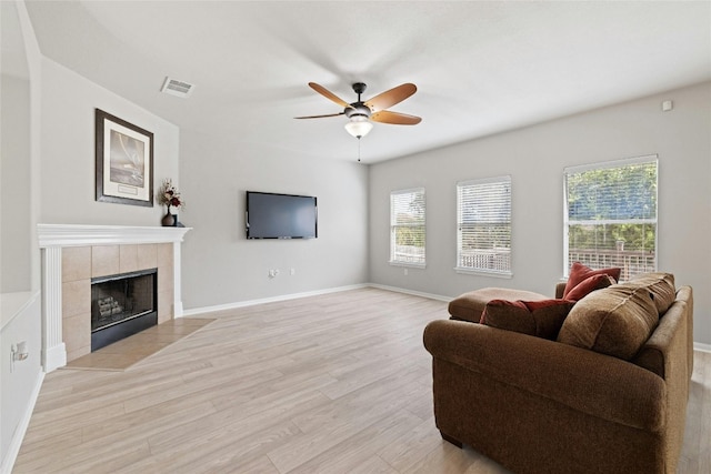 living room with a tiled fireplace, light wood-type flooring, and ceiling fan