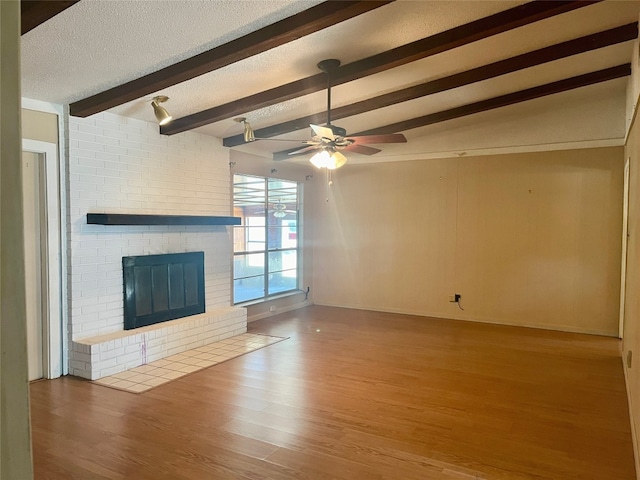 unfurnished living room with vaulted ceiling with beams, ceiling fan, hardwood / wood-style floors, a fireplace, and a textured ceiling