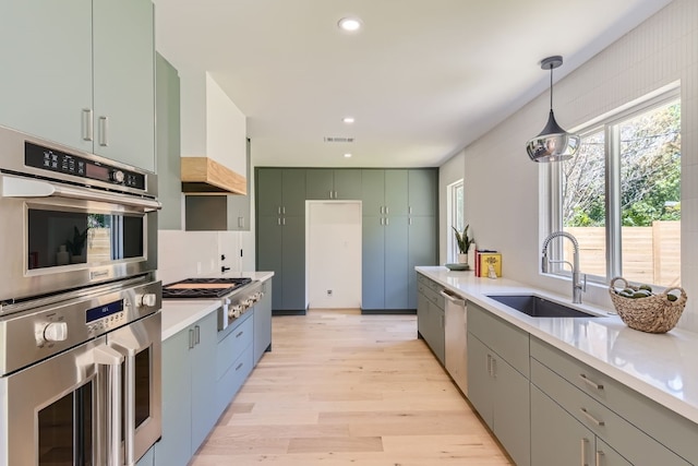 kitchen with appliances with stainless steel finishes, light hardwood / wood-style flooring, custom range hood, sink, and pendant lighting