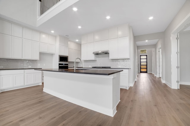 kitchen with white cabinets, a kitchen island with sink, built in microwave, and sink