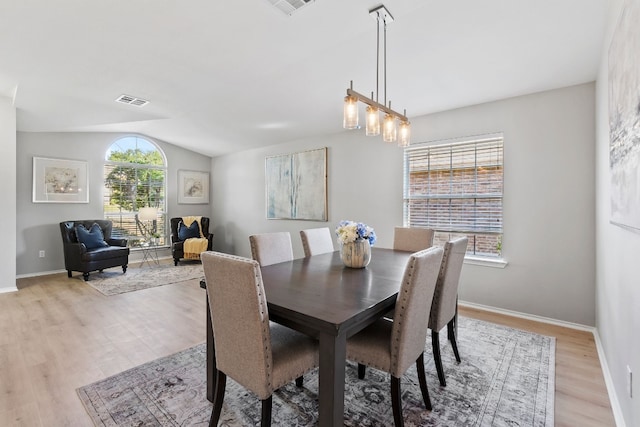 dining area with light wood-type flooring, vaulted ceiling, and a notable chandelier