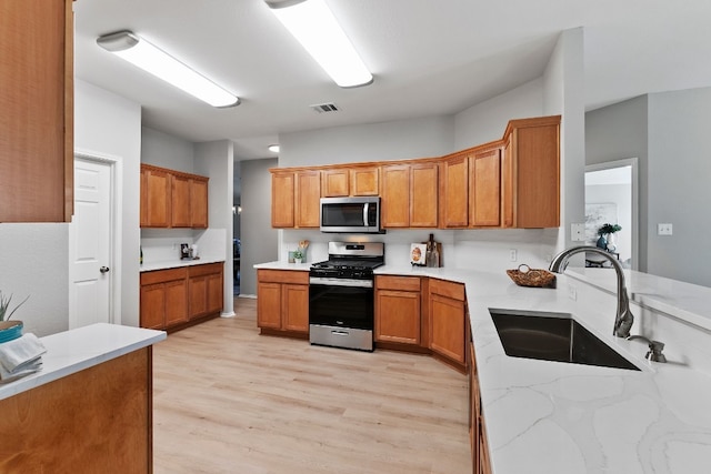 kitchen with sink, stainless steel appliances, light hardwood / wood-style flooring, and light stone counters