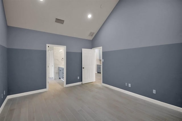 unfurnished bedroom featuring light wood finished floors, visible vents, connected bathroom, high vaulted ceiling, and baseboards