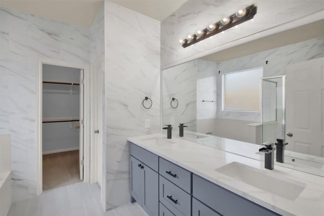 bathroom featuring a spacious closet, double vanity, a sink, and tile walls