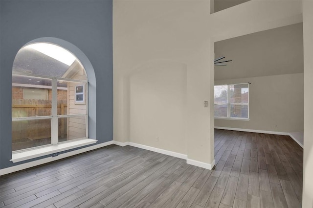 empty room with high vaulted ceiling, baseboards, and wood finished floors