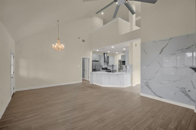 unfurnished living room with ceiling fan with notable chandelier, vaulted ceiling, baseboards, and wood finished floors