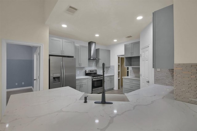 kitchen featuring wall chimney exhaust hood, appliances with stainless steel finishes, gray cabinets, and light stone counters