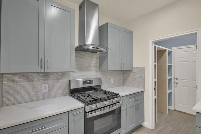 kitchen with light stone counters, stainless steel range with gas cooktop, gray cabinets, and wall chimney exhaust hood