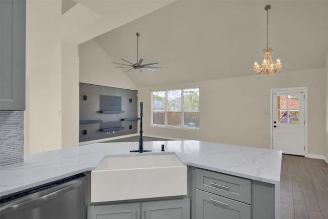 kitchen featuring open floor plan, light stone countertops, gray cabinetry, stainless steel dishwasher, and a sink