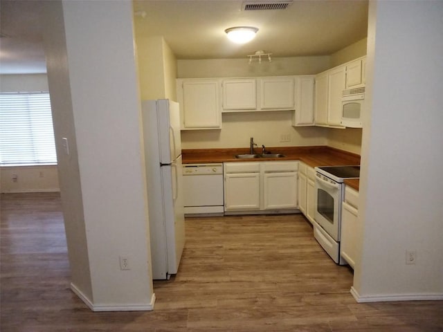 kitchen featuring dark countertops, white cabinetry, a sink, wood finished floors, and white appliances